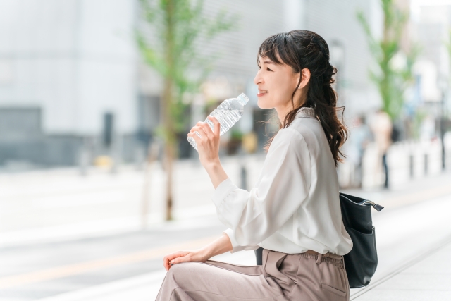 暑い中外回り中に水分補給する営業職の女性
